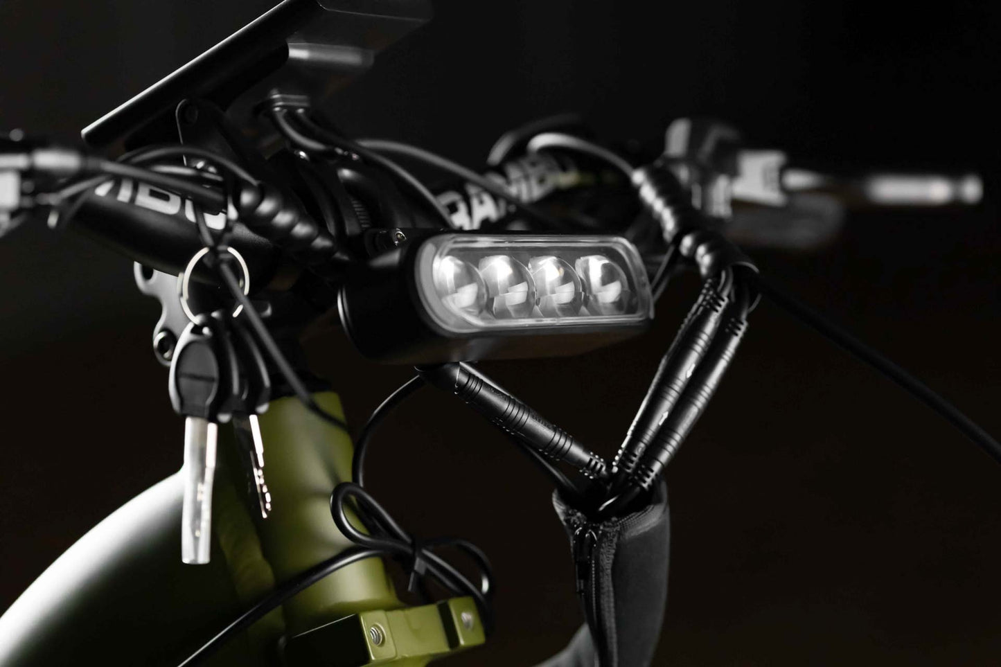 Close-up of a Rambo Bikes REBEL 2.0 Electric Bike handlebar with a light, keys, and a lock on a dark background