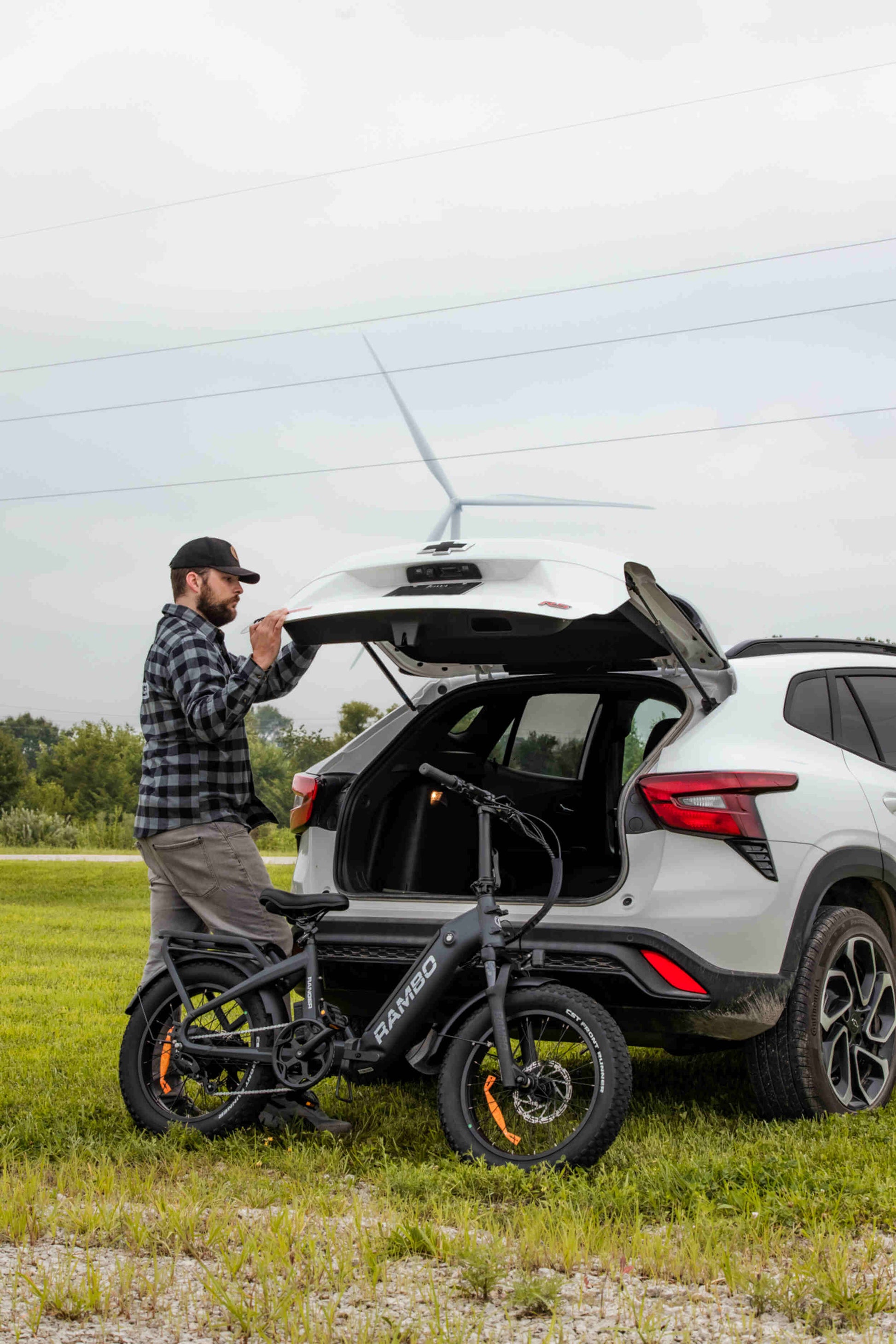 A man loading a Rambo Bikes RANGER Folding eBike into the back of a vehicle on a grassy field.