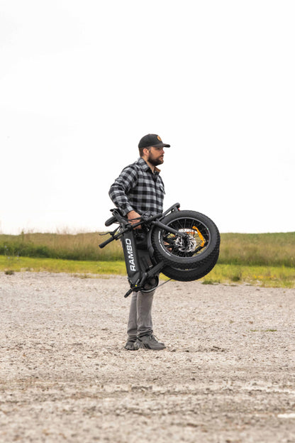 Person lifting the Rambo Bikes RANGER Folding eBike, demonstrating its portability and rugged design.