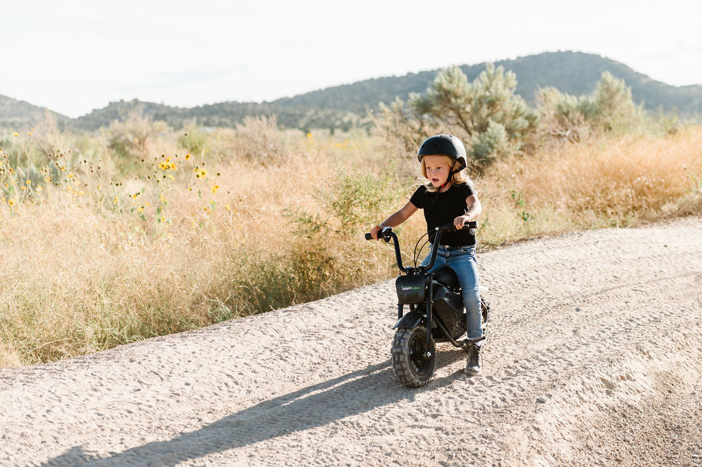 Child riding a Drift Hero USA 250W Mini Electric Bike on a dirt road with mountains in the background