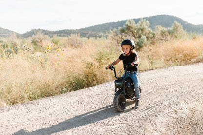 Child riding a Drift Hero USA 250W Mini Electric Bike on a dirt road with mountains in the background