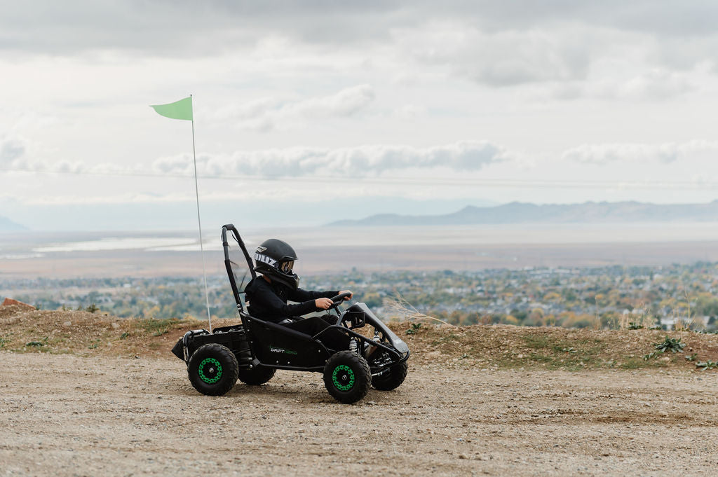 A kid driving a Drift Hero USA 1 Seater Electric Go-kart on a dirt track with a scenic background