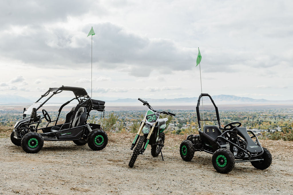 Two off-road vehicles and a Drift Hero USA 1 Seater Electric Go-kart on a dirt road with a scenic background