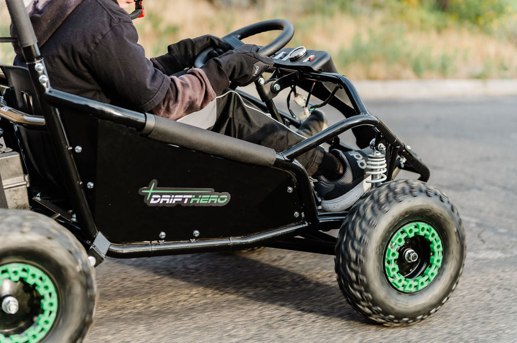 Person driving a Drift Hero USA 1 Seater Electric Go-kart  with green wheels on a paved road.