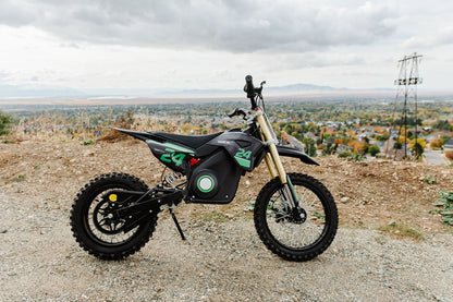 Drift Hero USA 1600W Electric Dirt Bike on a gravel hill with a cityscape in the background