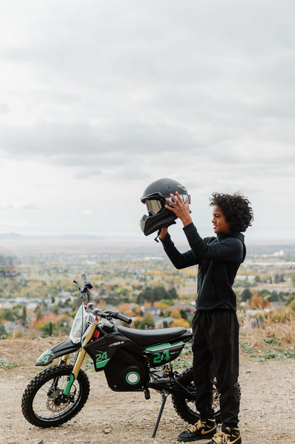 Person holding a helmet next to a Drift Hero USA 1600W Electric Dirt Bike on a scenic background