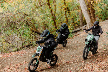 Three people riding Drift Hero USA 1600W Electric Dirt Bike on a forest trail