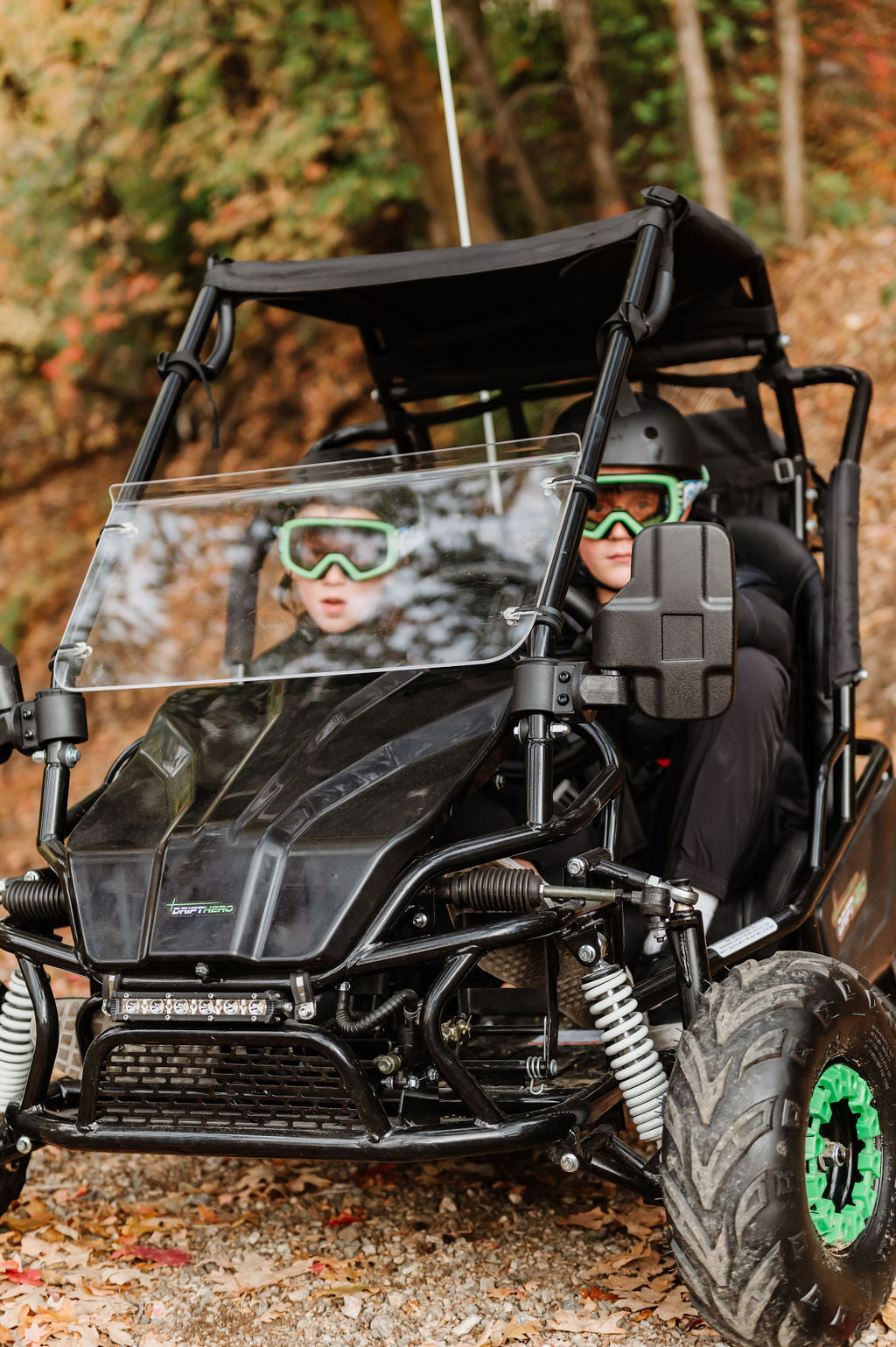 Two people in aDrift Hero USA 2 Seater Electric Go-kart  with green accents on a trail in the forest with trees in the background