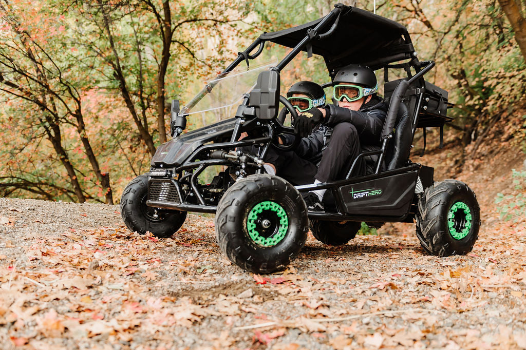 Two people in aDrift Hero USA 2 Seater Electric Go-kart  with green accents on a forest trail.