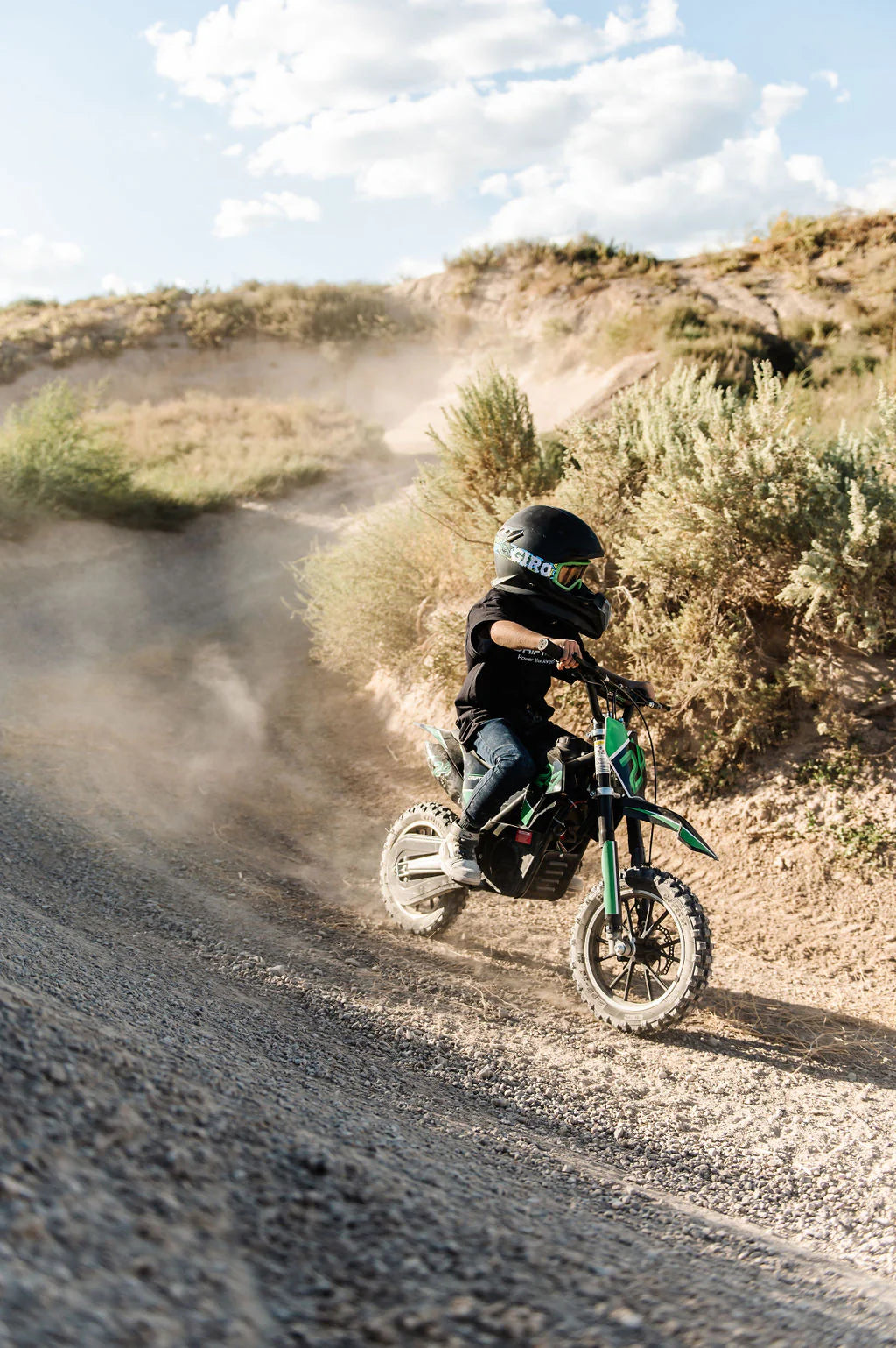 Child riding a Drift Hero USA 800W Electric dirt bike on a dusty trail with a helmet