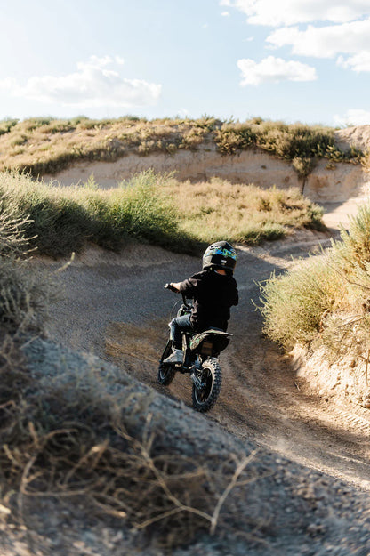 Kid riding a Drift Hero USA 800W Electric dirt bike on a desert trail with a helmet.