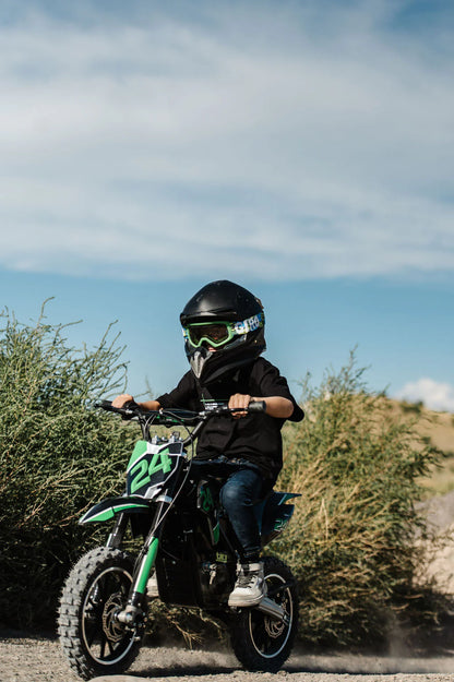 Child riding a Drift Hero USA 800W Electric dirt bike with a helmet and goggles on a dirt path.