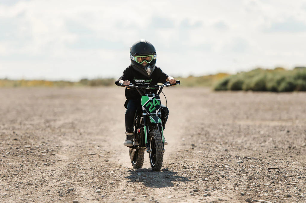 Child riding a Drift Hero USA 800W Electric dirt bike on a dirt track with a helmet and goggles.