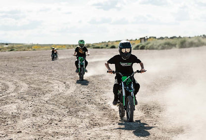 Three kids riding Drift Hero USA 800W Electric dirt bike on a dusty track with a clear sky.