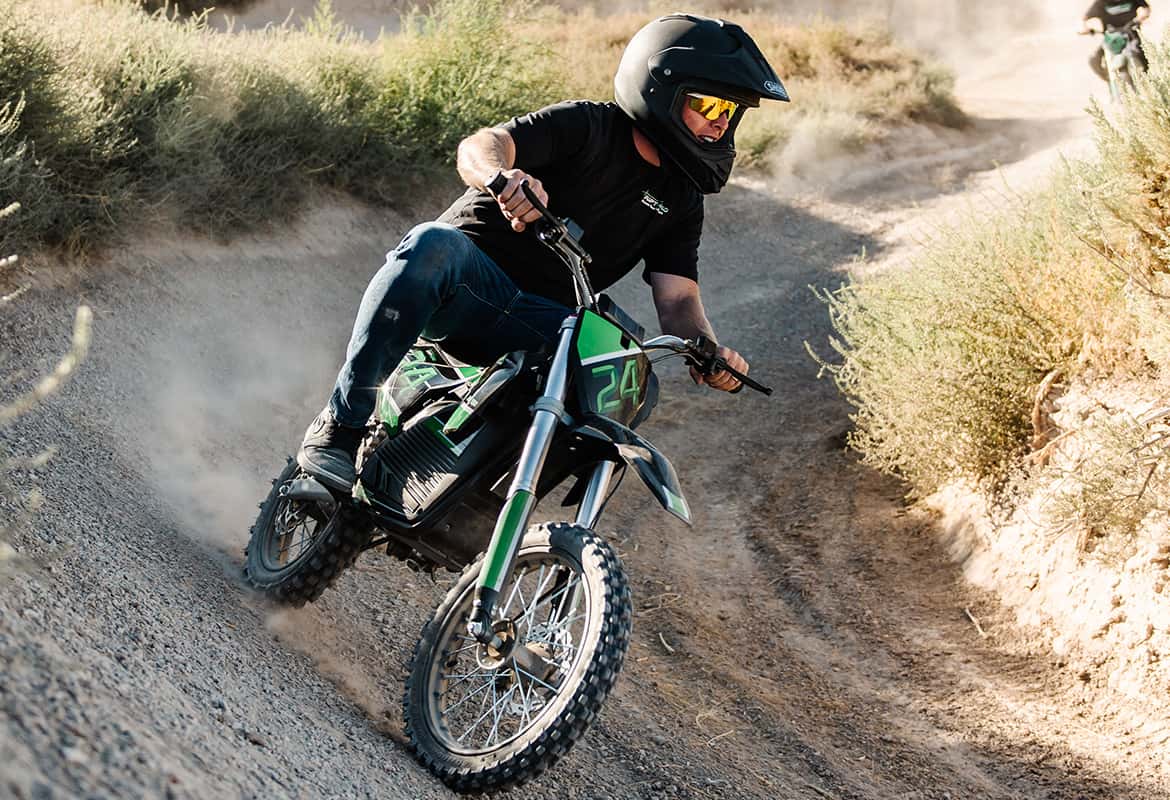 Person riding a Drift Hero USA 800W Electric dirt bike on a dusty trail with a helmet and goggles.