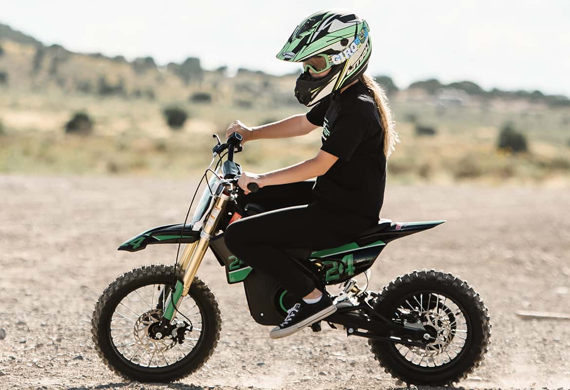 Teen riding a Drift Hero USA 800W Electric dirt bike in an open field wearing a helmet and black outfit.