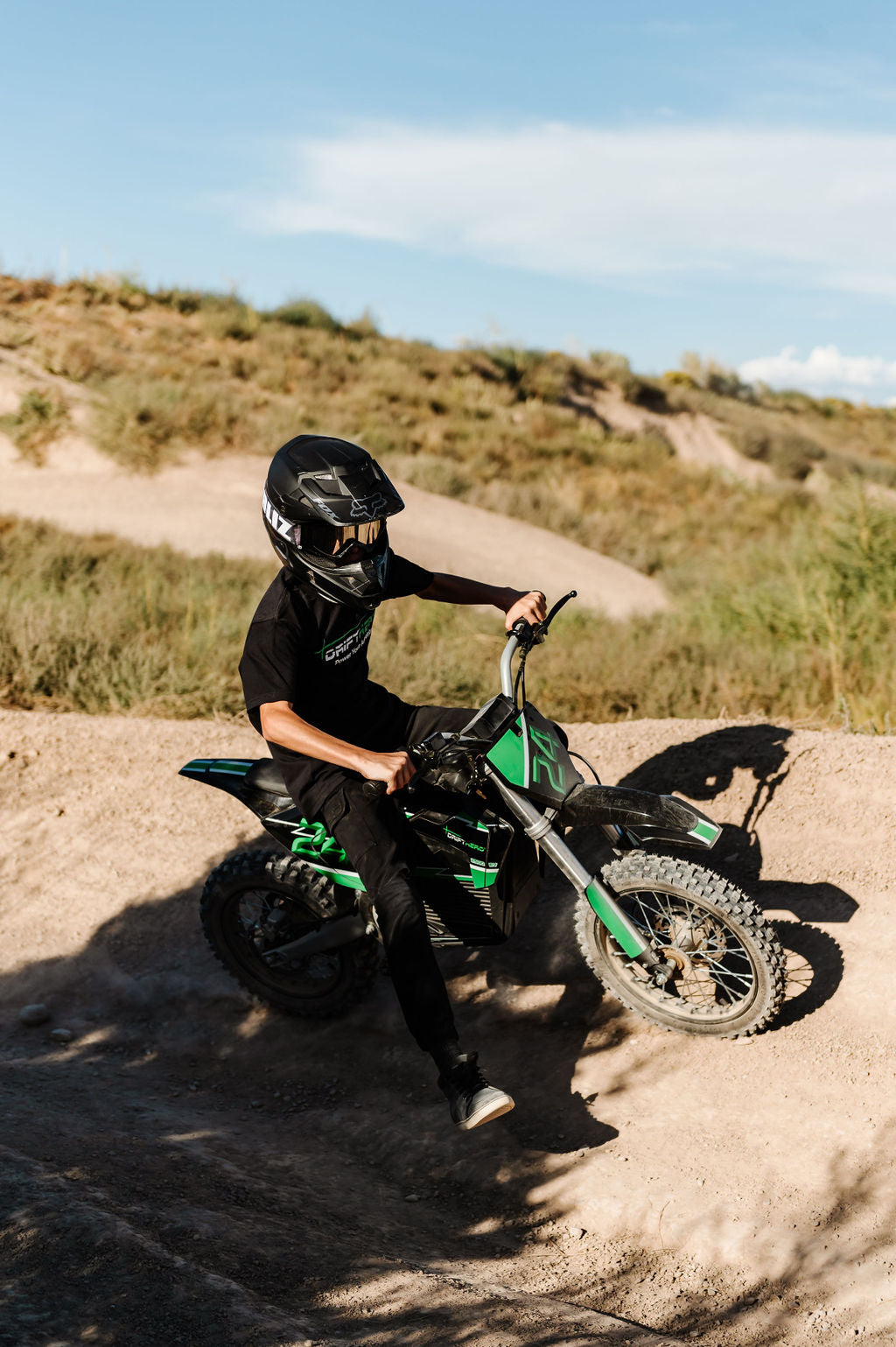 Rider on green electric dirt bike turning on dirt berm trail