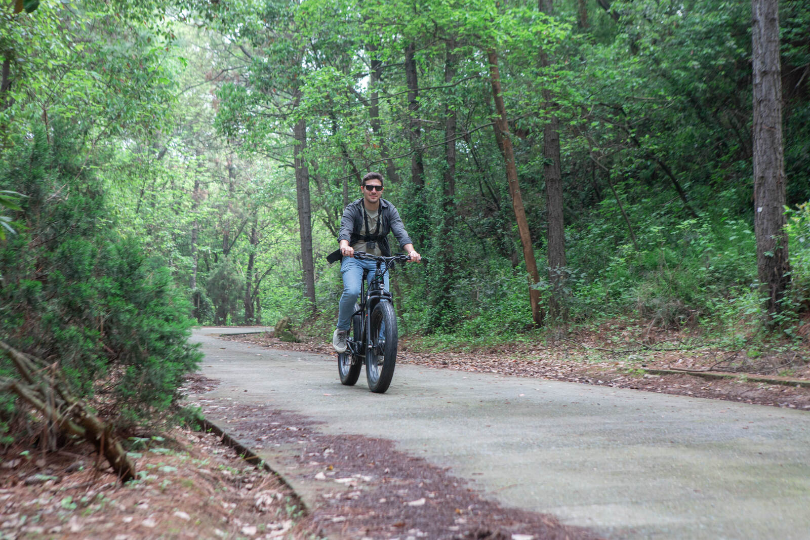 Eunorau FAT AWD 2.0 electric bike in black, male rider cycling on a forest trail surrounded by green trees.