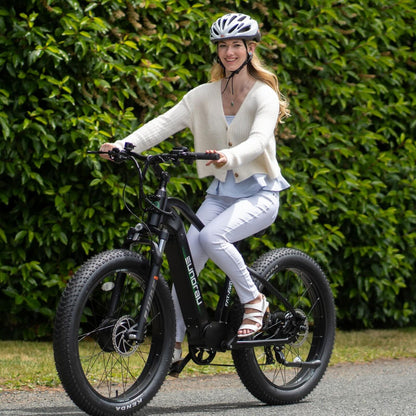 Eunorau FAT AWD 2.0 electric bike in black, outdoor riding shot with female rider wearing helmet on a paved road.
