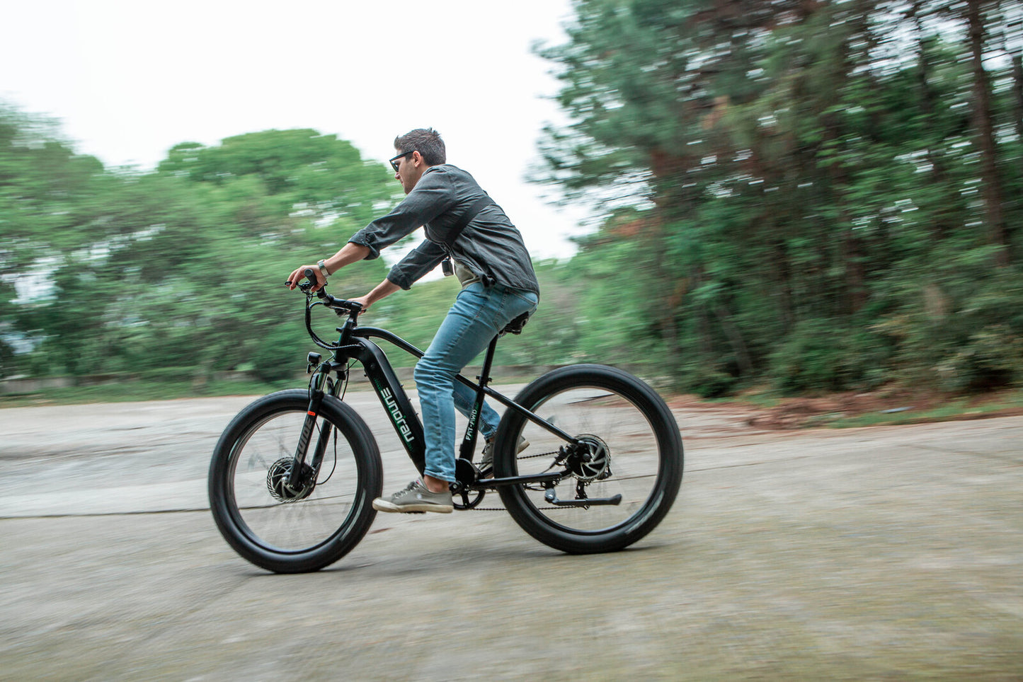 Male cycler on a Eunorau FAT AWD 2.0 black ebike cycling on a forest trail with trees in the background