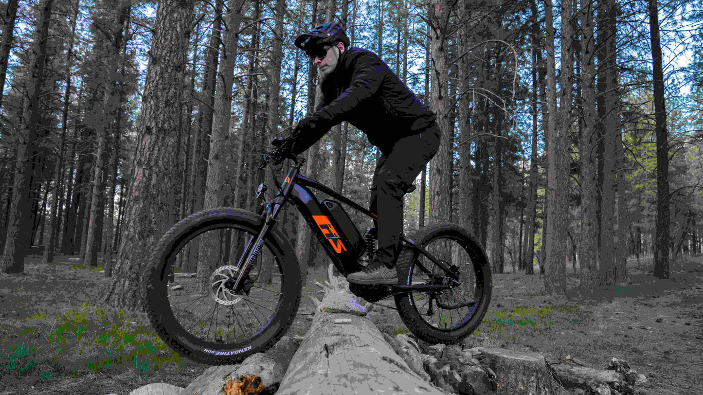 Eunorau Fat-HS electric fat tire bike with rider balancing on a large fallen log along a forest trail.
