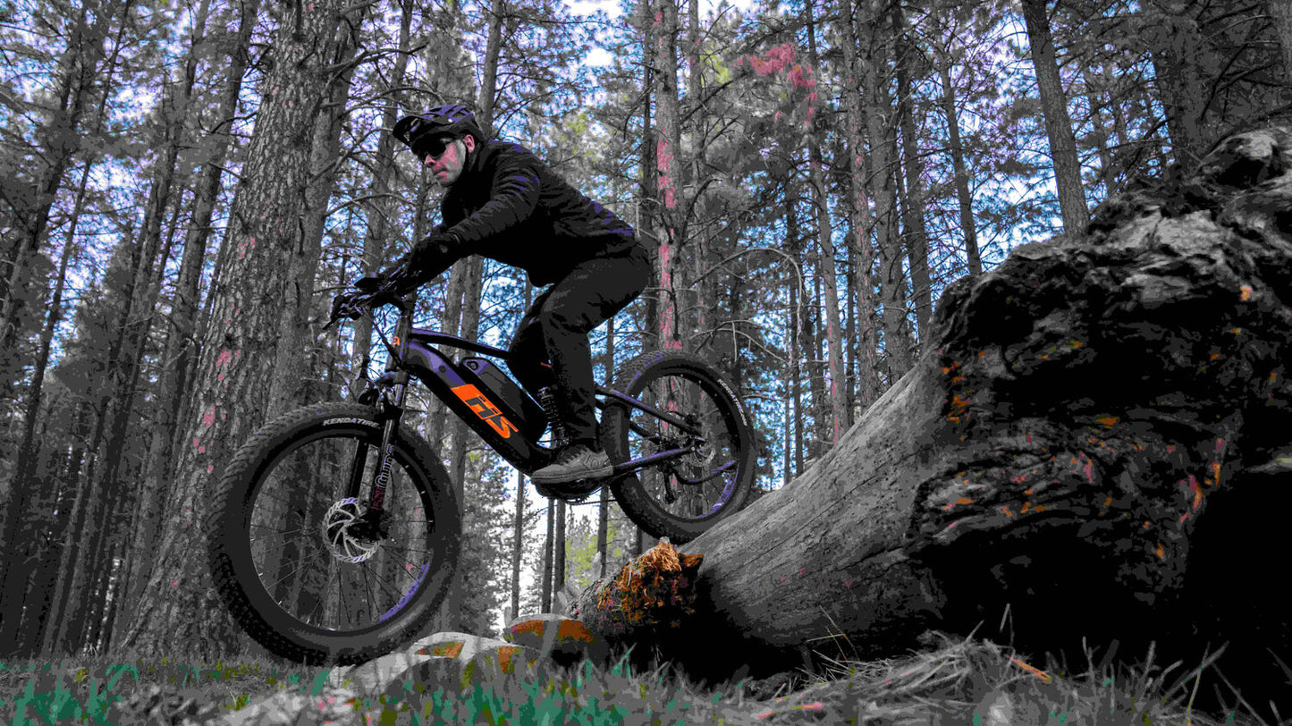 Eunorau Fat-HS electric fat tire bike side profile crossing a fallen log in dense forest terrain.
