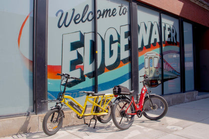 Two Eunorau G30 Cargo electric bicycles, one yellow and one red, parked in front of a store with 'Welcome to Edge Water' sign.