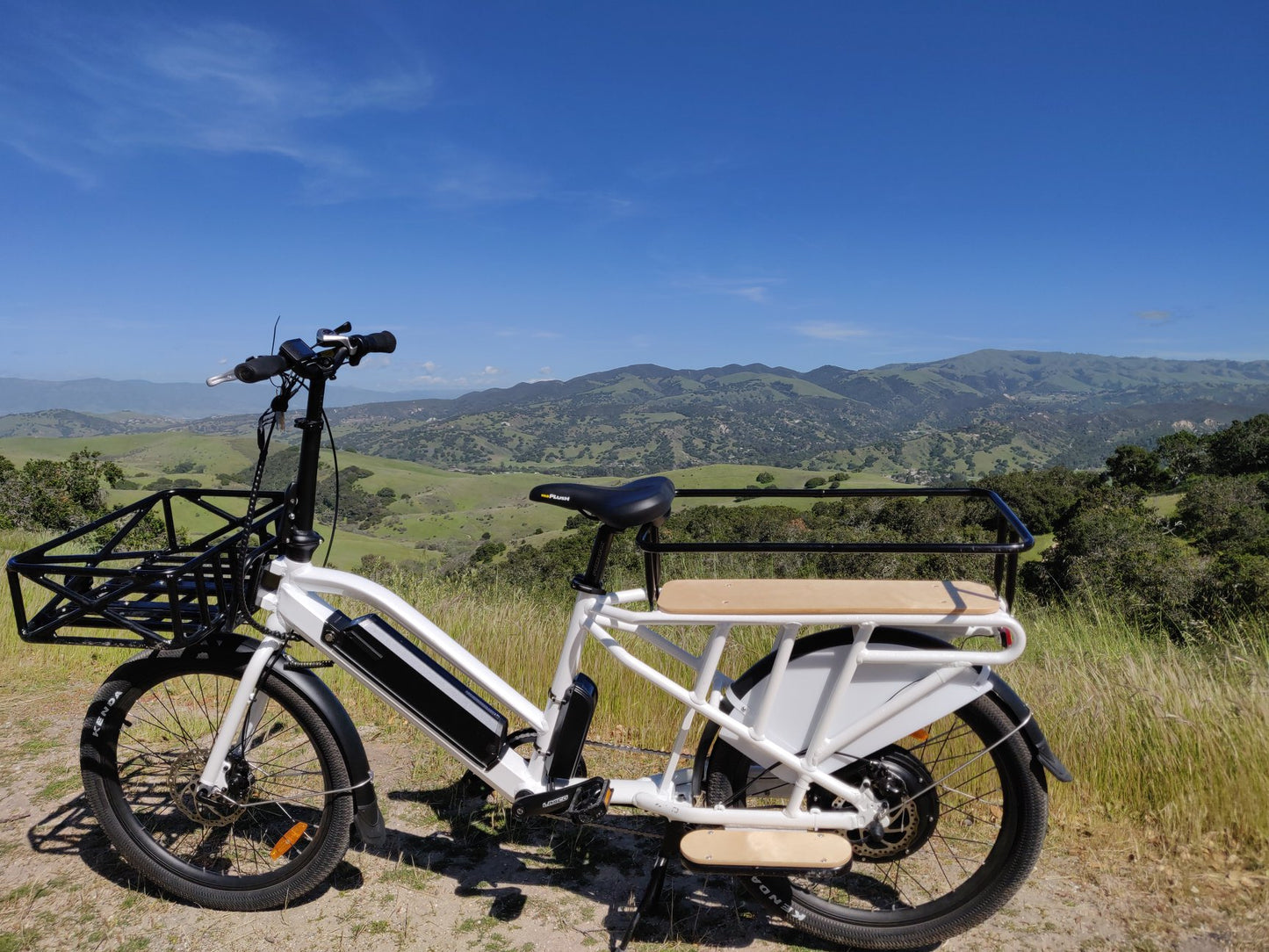 White Eunorau Max-Cargo 14AH with a wooden seat and basket on a grassy hill with mountains in the background