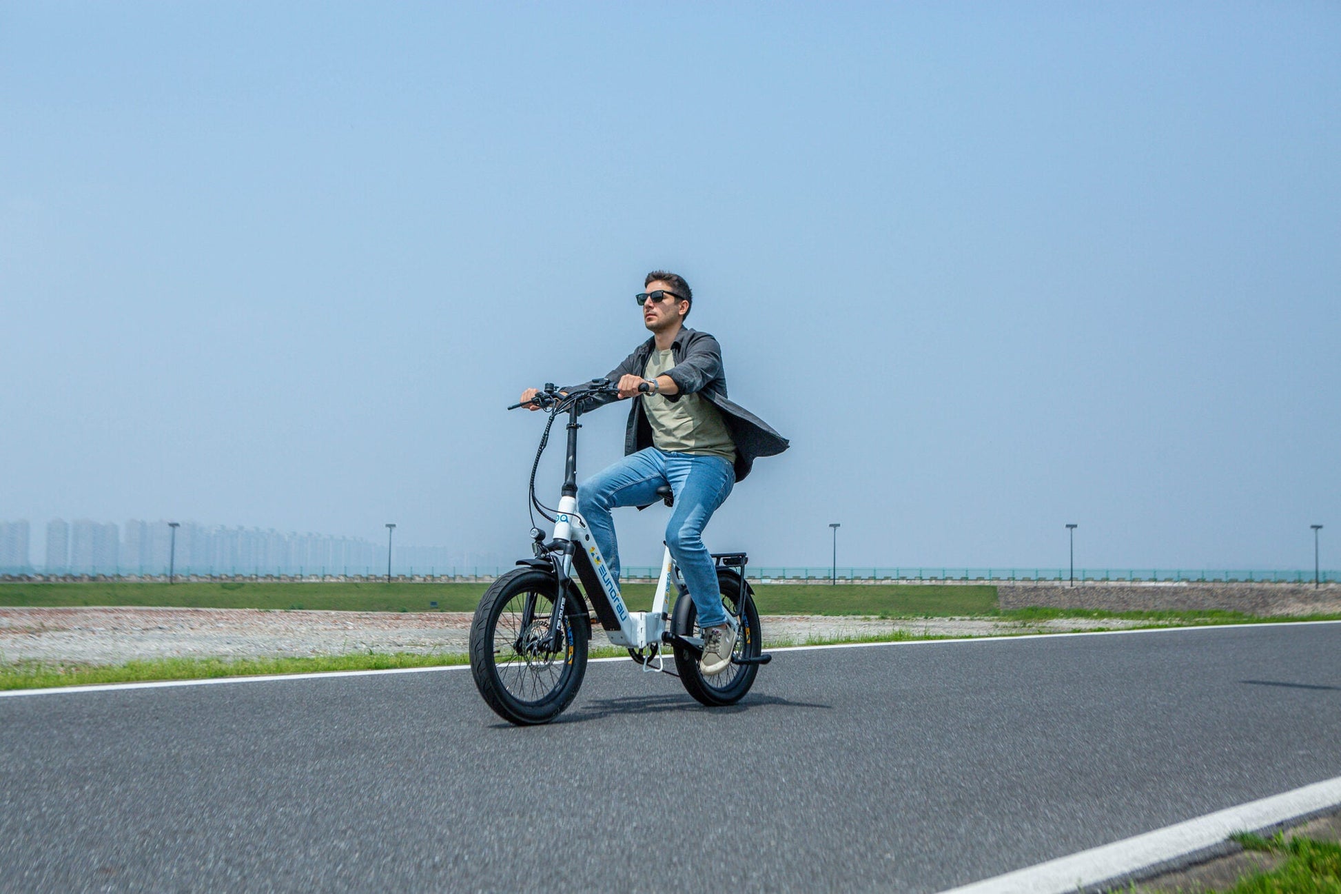 Man riding a white EUNORAU META Foldable electric bike on a paved road with clear blue sky background