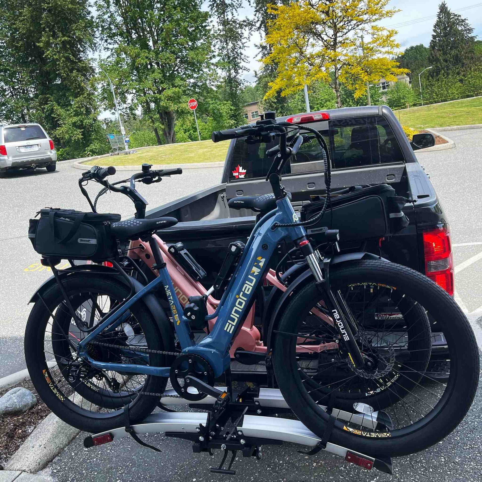 Eunorau Meta 24 ST 2.0 Electric bike  on a bike rack attached to a vehicle in a parking lot with trees and a stop sign in the background.
