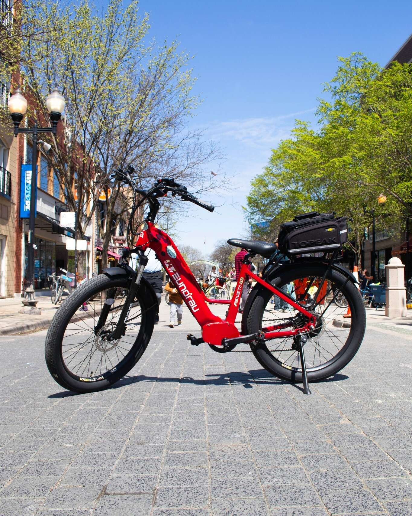 Eunorau Meta 24 ST 2.0 Red Electric bike on a city street with buildings and trees in the background