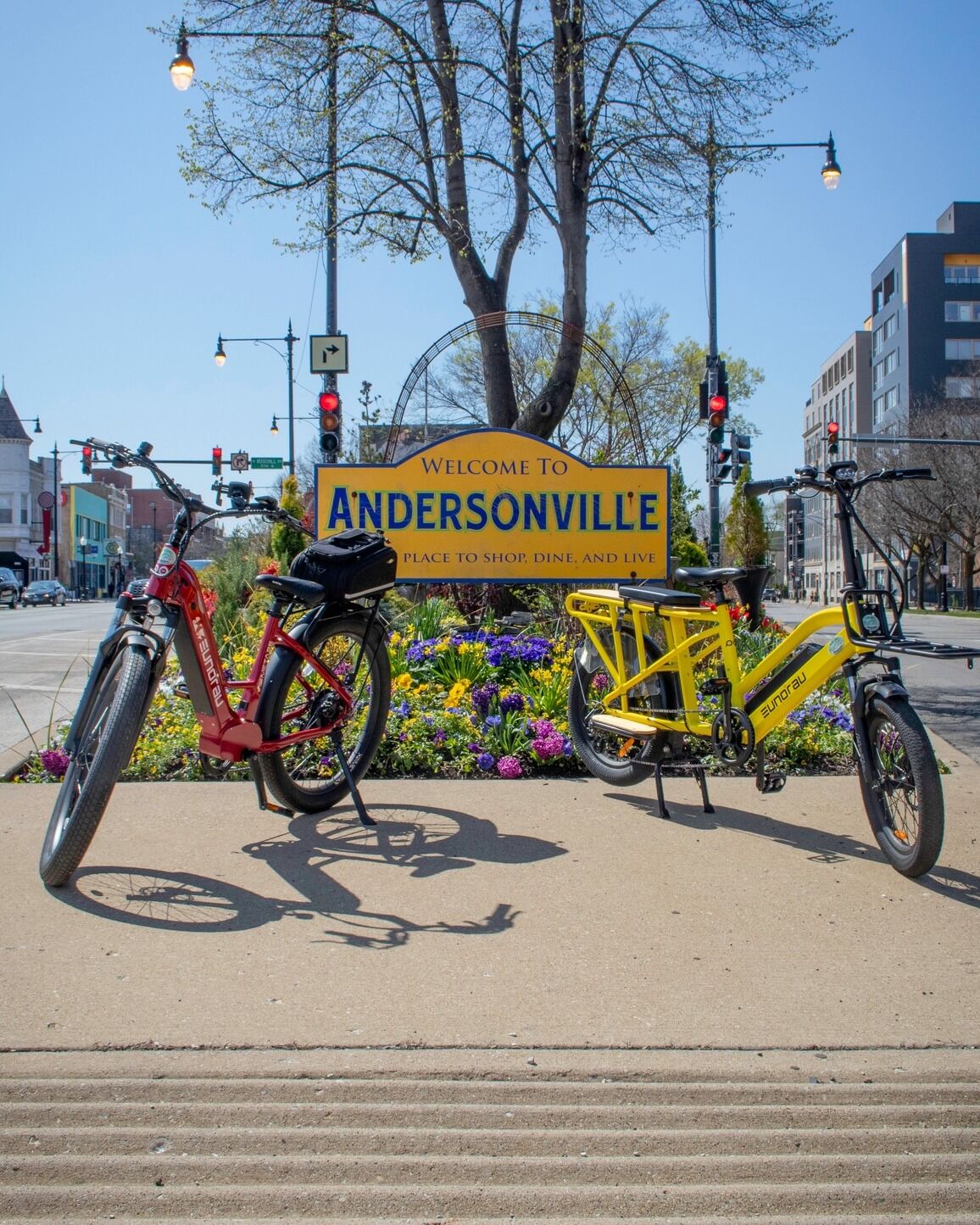 Eunorau Meta 24 ST 2.0  Two Electric bicycles parked on a sidewalk with a 'Welcome to Andersonville' sign in the background.