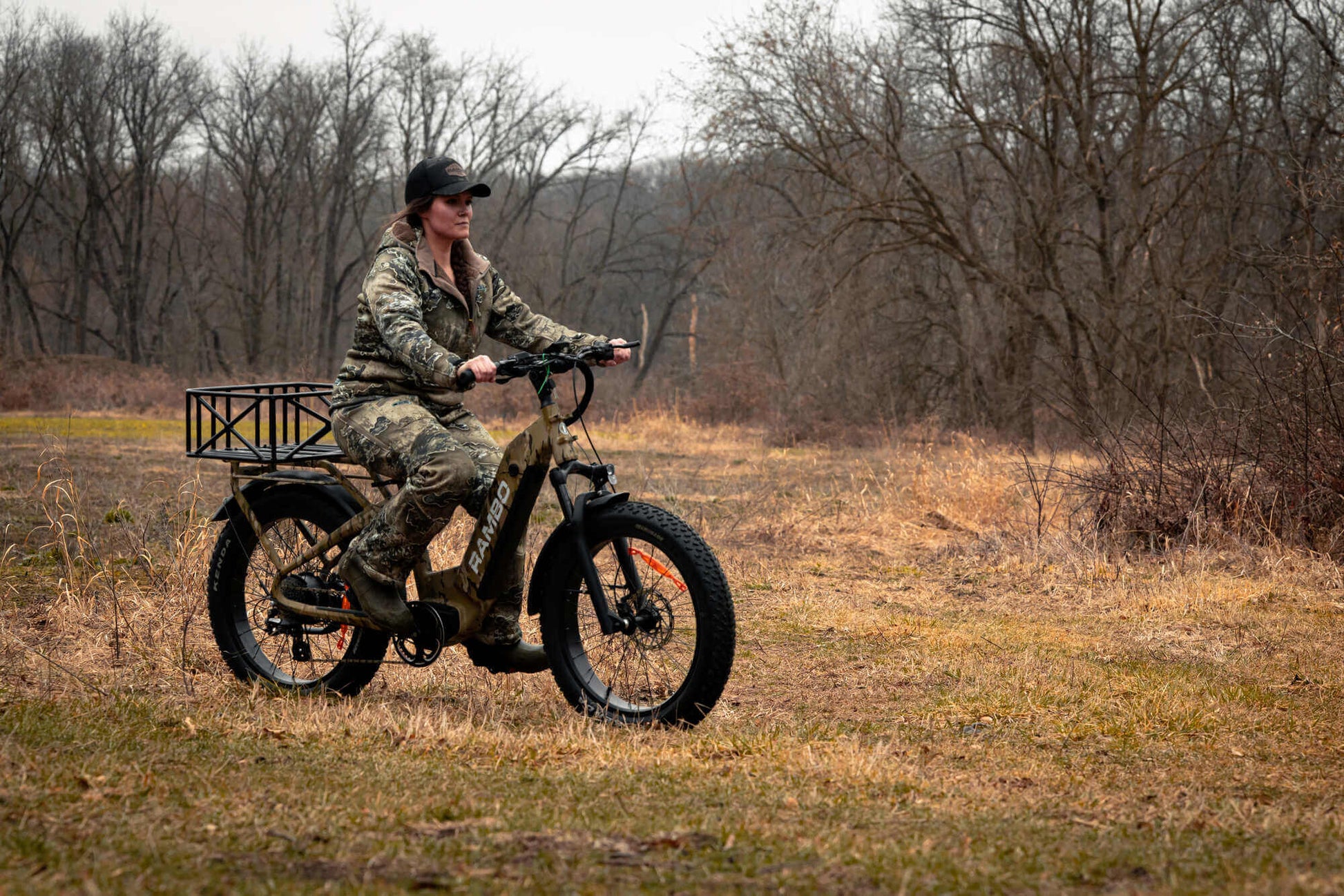 Person riding a Rambo Bikes SAVAGE 2.0 Electric Bike in a field with bare trees in the background