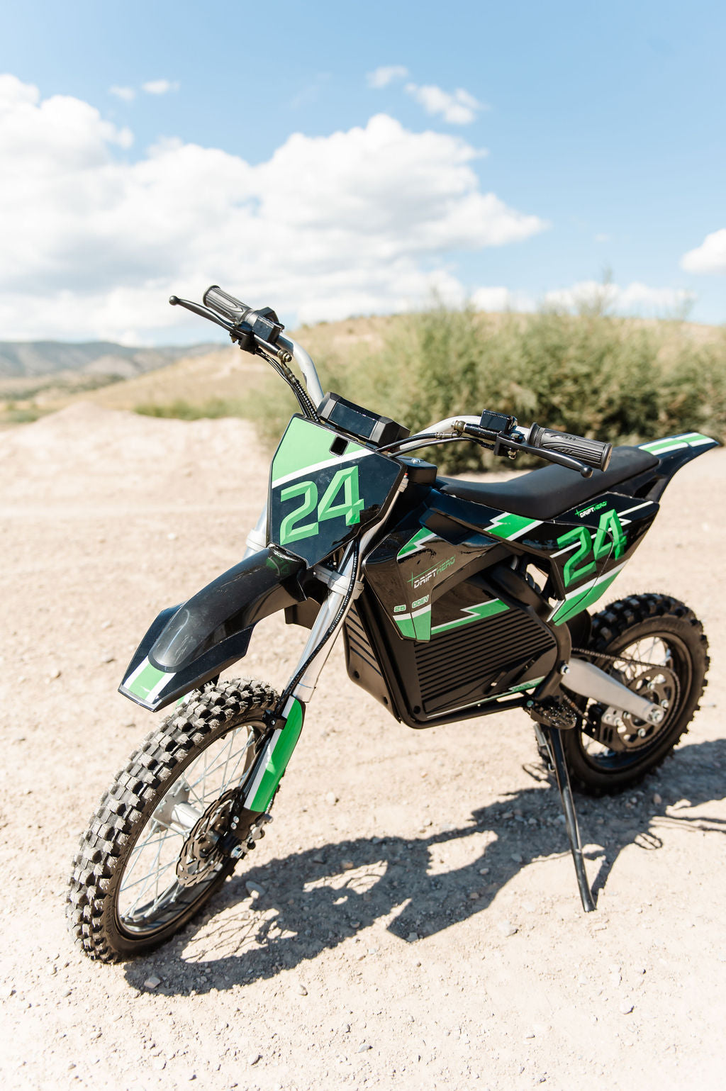 Green and Drift Hero USA 2500W Electric Dirt Bike with number 24 on a dirt road under a blue sky.