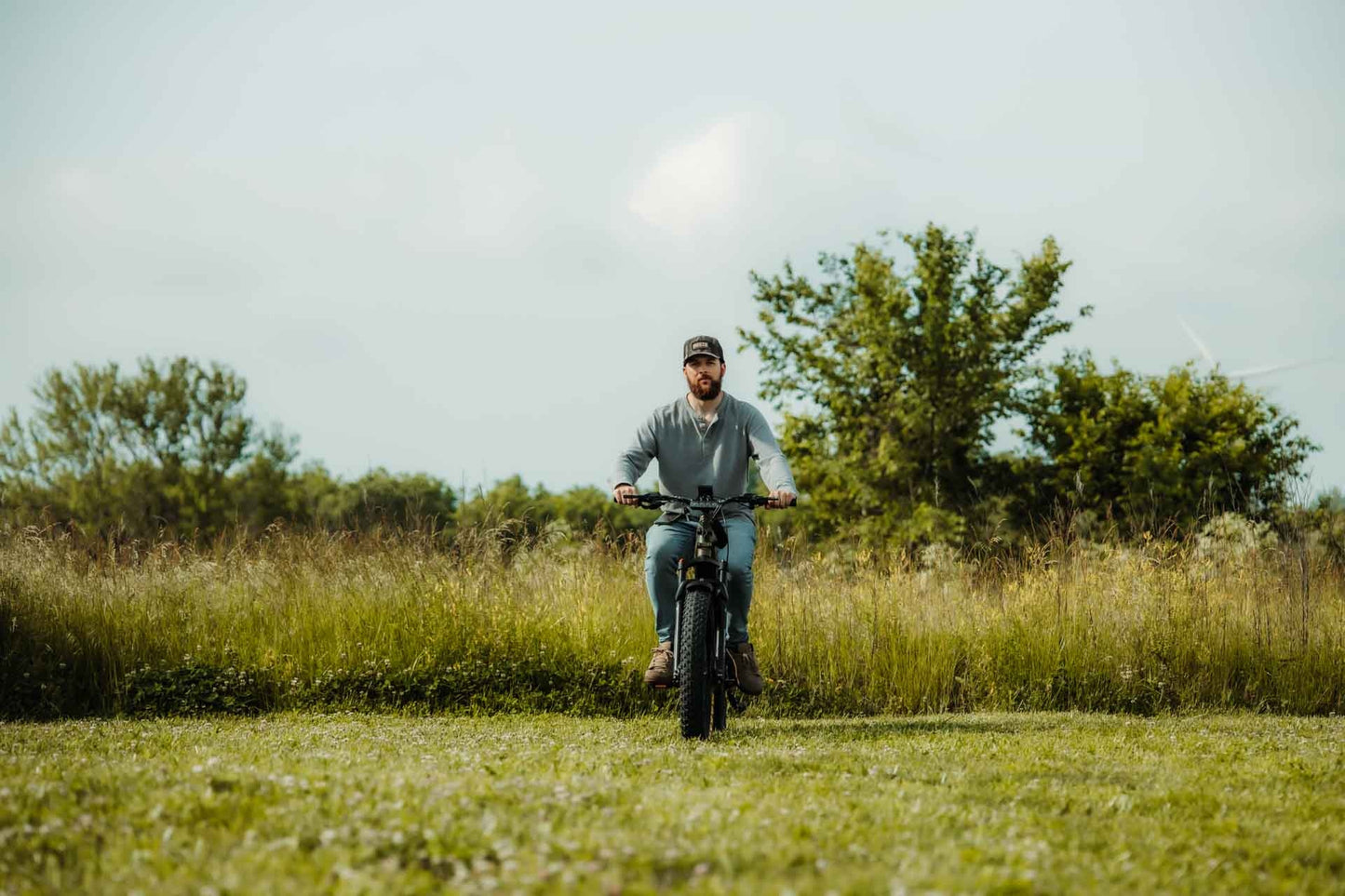 Man riding a Rambo Bikes REBEL 2.0 Electric Bike in a grassy field with trees in the background