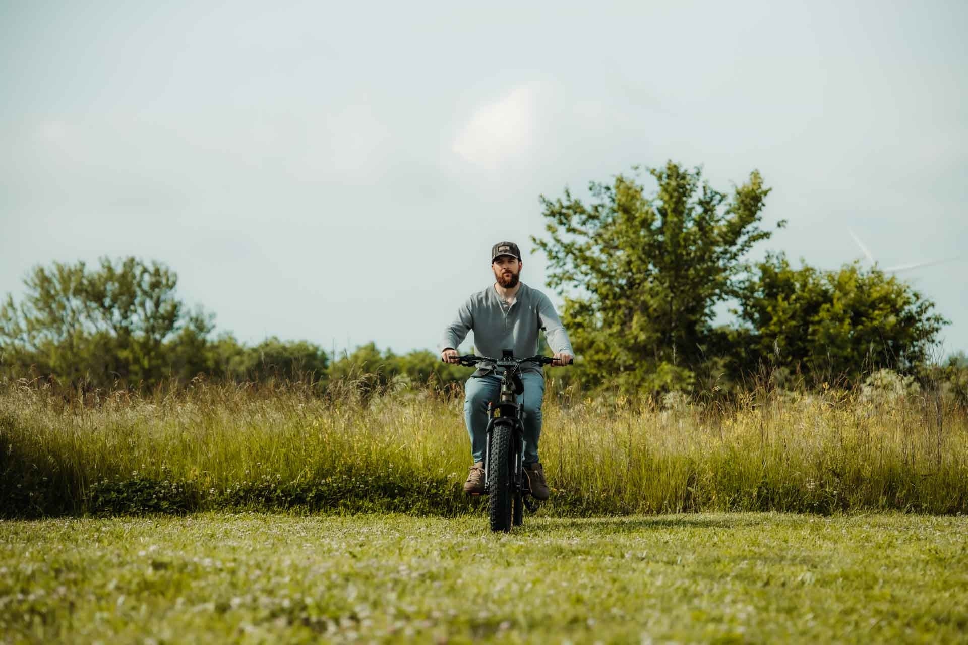Man riding a Rambo Bikes REBEL 2.0 Electric Bike in a grassy field with trees in the background