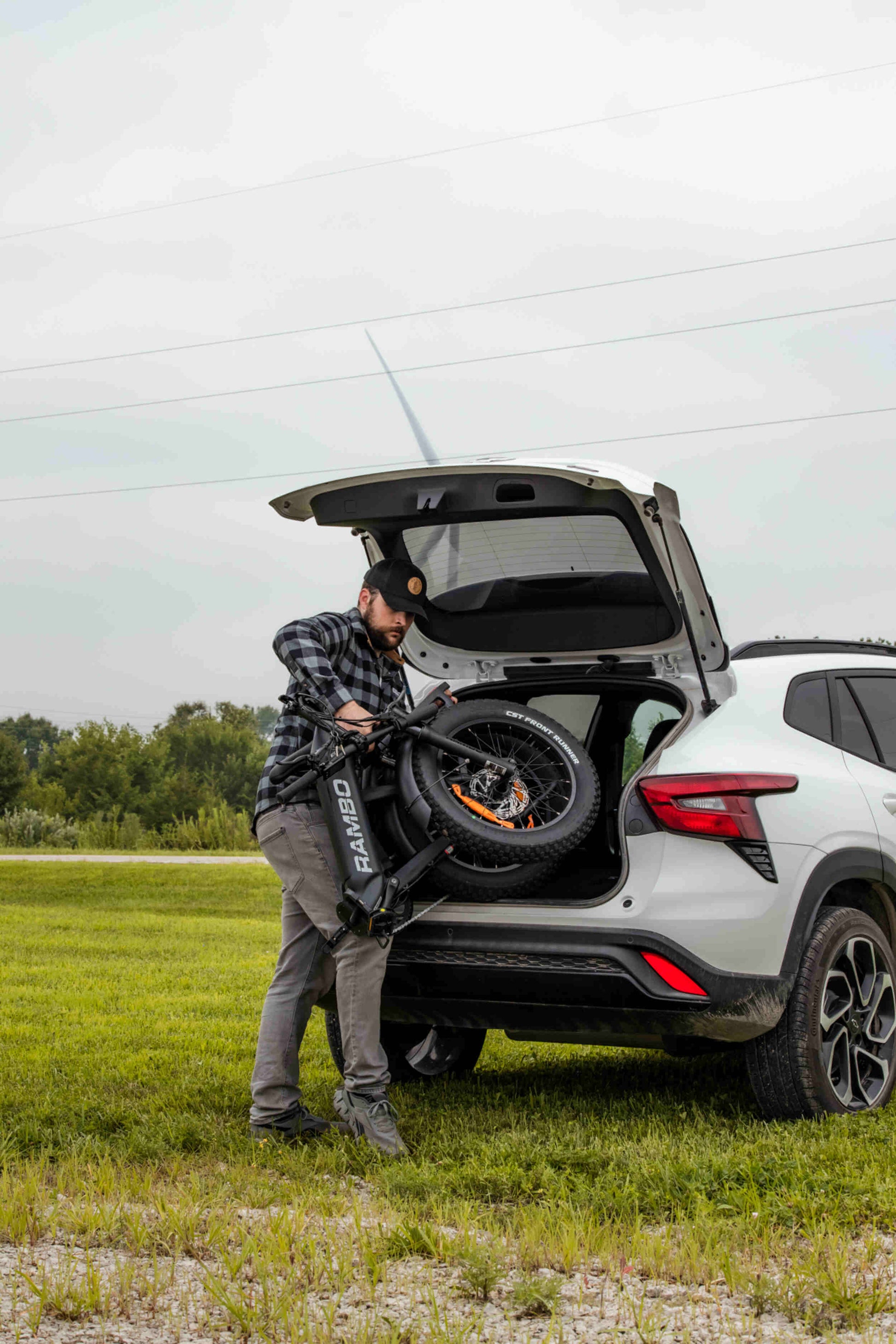 Man loading a Rambo Bikes RANGER Folding Electric Bike into a car trunk in a field