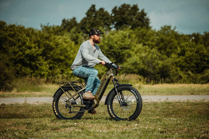 Man riding a large wheel Rambo Bikes REBEL 2.0 Electric Bike in a natural setting with trees and grass.