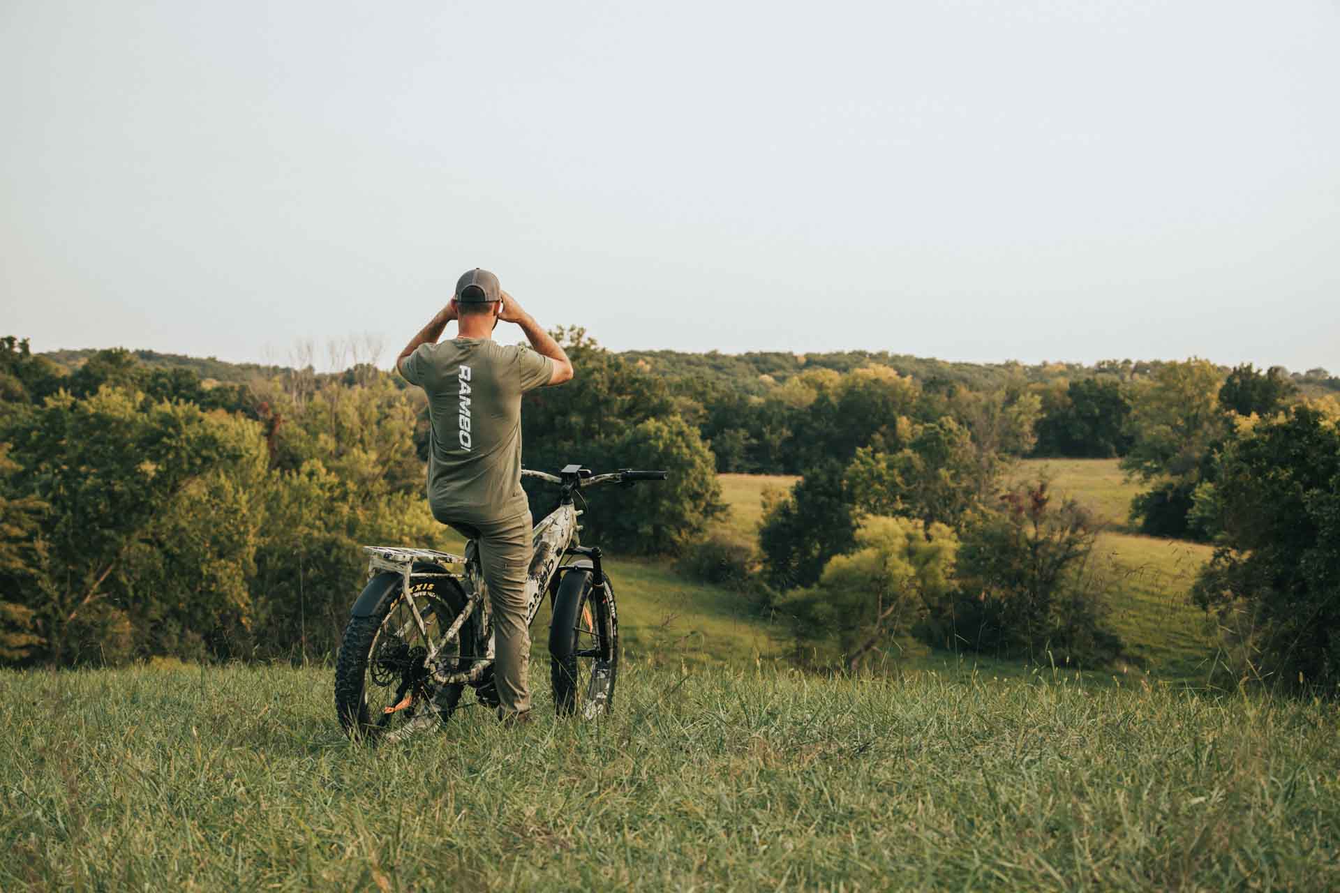 Person sitting on a Rambo Bikes Venom 2.0 Electric Bike in a grassy field with trees in the background