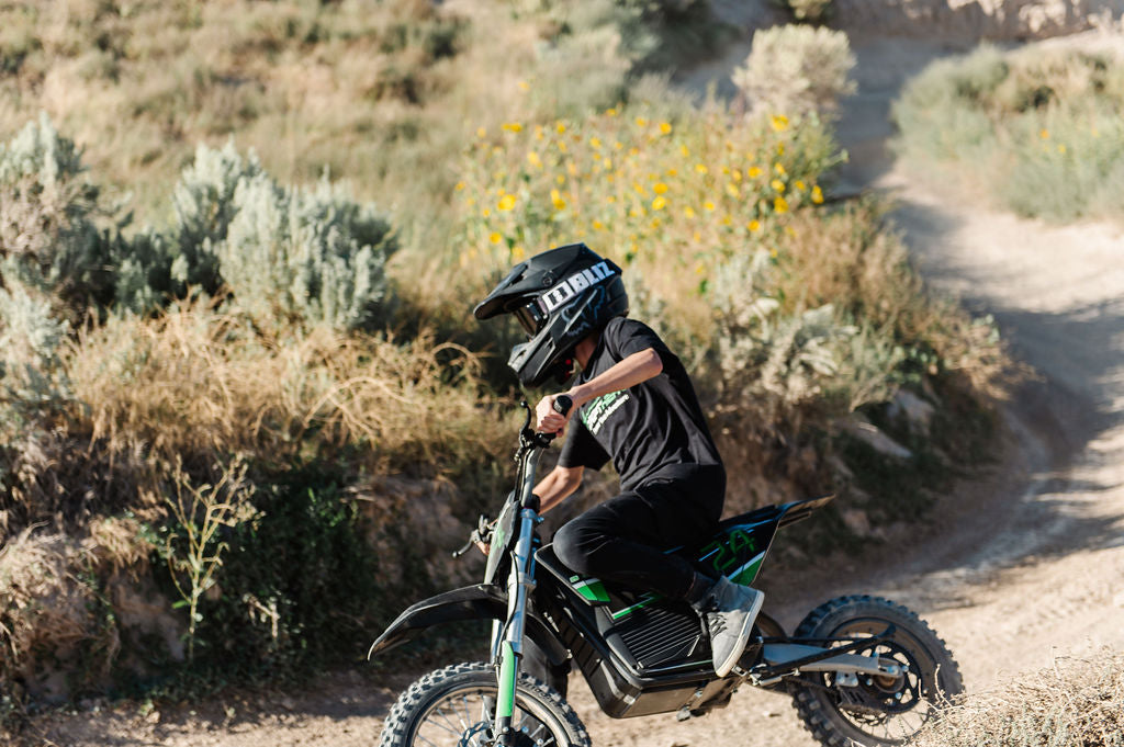 Person riding a Drift Hero USA 2500W Electric Dirt Bike in a desert-like environment with desert plants and a clear sky.