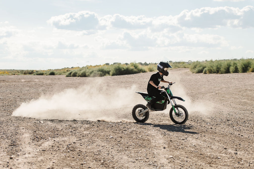 Person riding a Drift Hero USA 2500W Electric Dirt Bike on a dusty track with a clear sky.