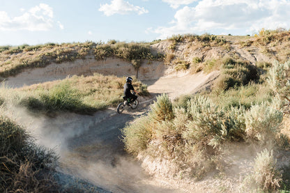 Person riding a Drift Hero USA 2500W Electric Dirt Bike on a dirt trail in a desert landscape with a clear sky.