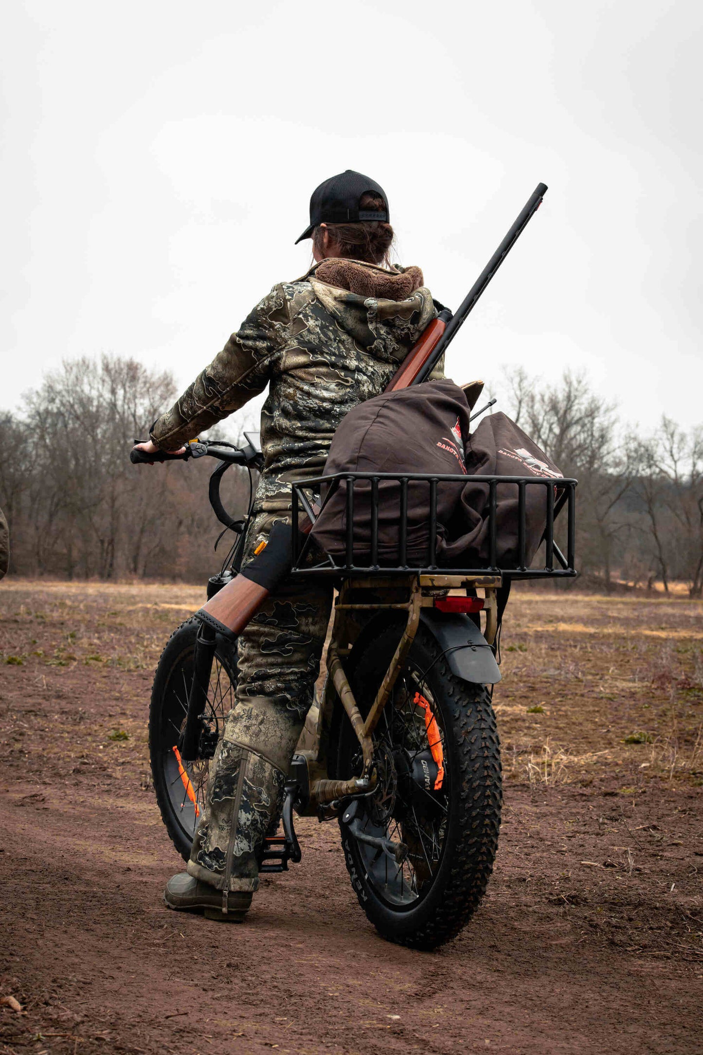 Person on a Rambo Bikes SAVAGE 2.0 Electric Bike with a large bag and rifle, riding through a field.
