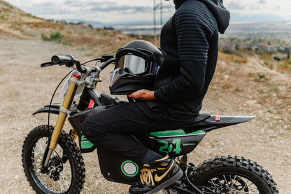 Person sitting on a Drift Hero USA 1600W Electric Dirt Bike with a helmet, wearing black gear, in an outdoor setting.