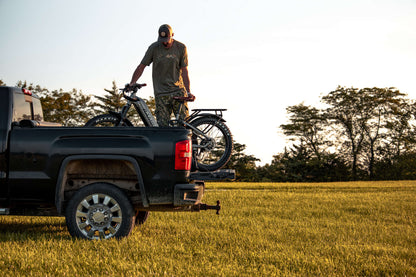 Man loading a Rambo Bike Hellcat 2.0 AWD Electric Bike onto the back of a black pickup truck in a field.