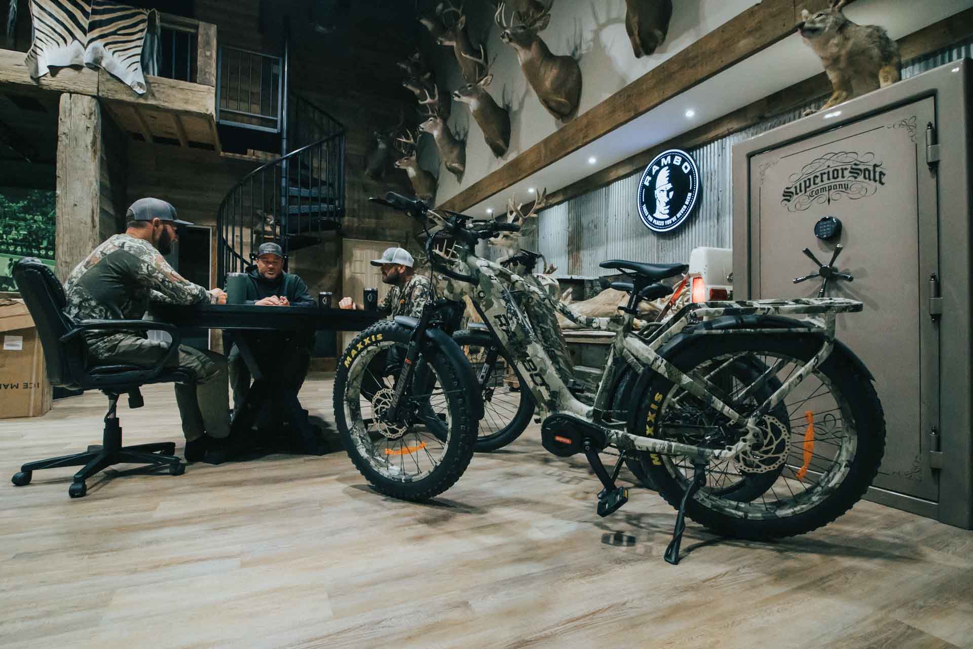 Two Rambo Bikes Venom 2.0 Electric Bike in a room with hunting decor and people sitting at a table.