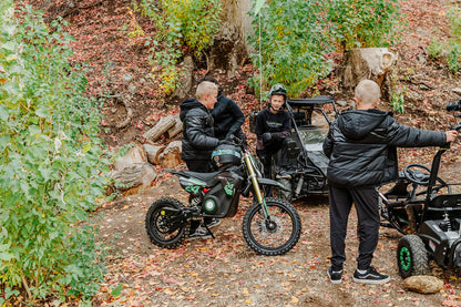 Three people with Drift Hero USA 1600W Electric Dirt Bike in a forest setting