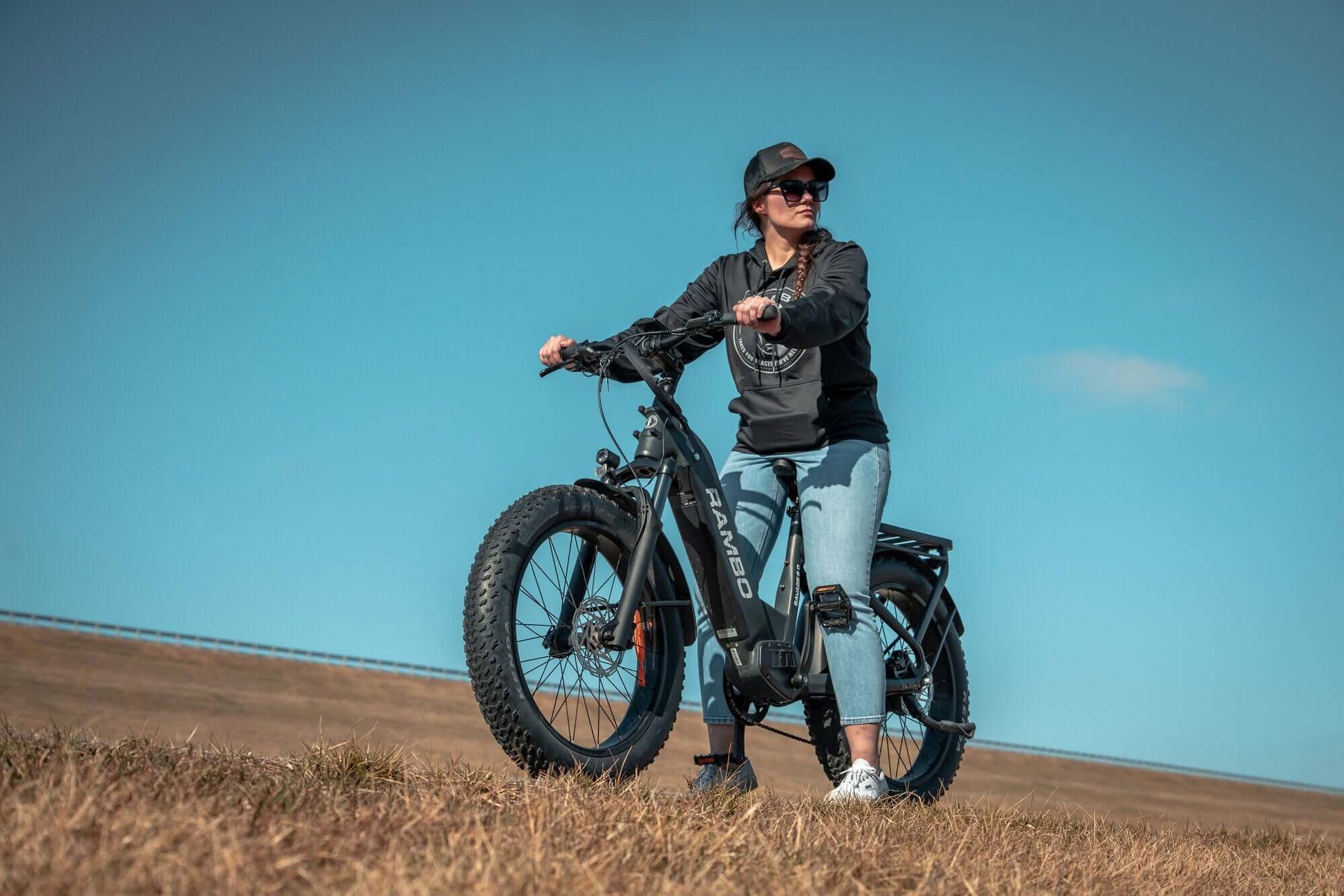 Person standing with an Rambo Bikes SAVAGE 2.0 Electric Bike in a field under a clear blue sky